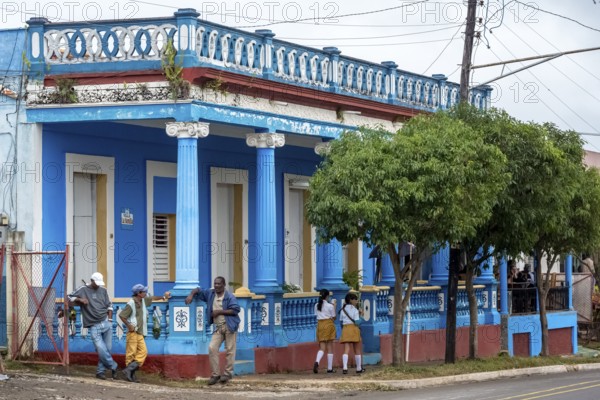 Typical Cuban blue house with columns, workers and girls in school uniform, Viñales, Cuba, Pinar