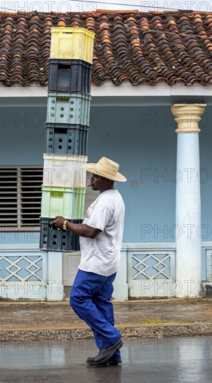 Cuban man with hat carrying and balancing crates of drinks across a street in Vinales, Viñales,