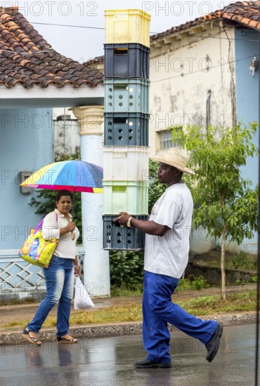 Cuban man with hat carrying and balancing crates of drinks across a street in Vinales, Viñales,