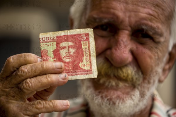 Old Cuban man holding a three peso banknote with the portrait of Ernesto Che Guevara in his hand,