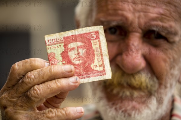Old Cuban man holding a three peso banknote with the portrait of Ernesto Che Guevara in his hand,