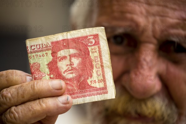 Old Cuban man holding a three peso banknote with the portrait of Ernesto Che Guevara in his hand,