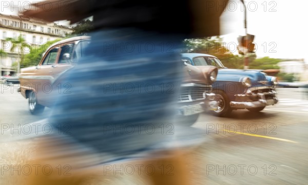 Part of a pedestrian in front of cars, speed, blurred, moving old car, vintage car in street scene,