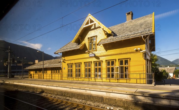Yellow wooden railway station building Vaksdal, railway tracks, blue sky, near Bergen city railway