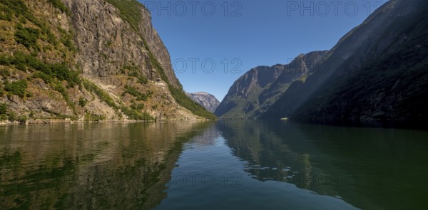An approaching excursion boat on a beautiful fjord reflecting the light, surrounded by rocks partly