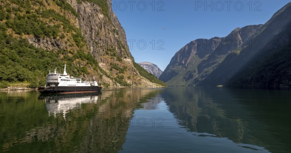 An approaching excursion boat on a beautiful fjord reflecting the light, surrounded by rocks partly