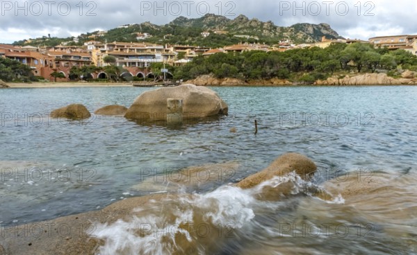 Sardinia, waves on the rocky coast, residential complex in the picturesque harbour town of Porto