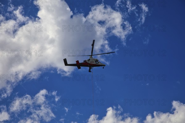 Small helicopter in the blue sky with few clouds, transport helicopter, timber transport, Saas