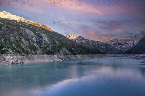 Early morning light over a lake with snow-covered mountains and pink sky, Mattmark reservoir, Saas