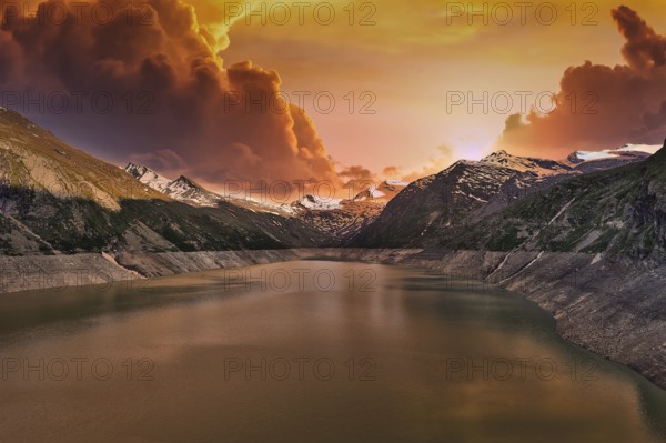 Mountain lake at sunset with dramatic clouds and orange sky, Mattmark reservoir, Saas Almagell,