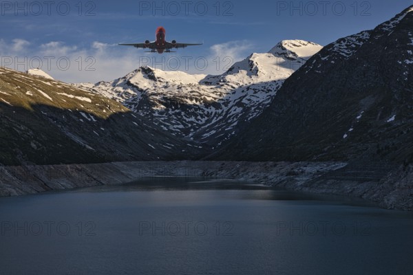 Aeroplane flying over a mountain lake with snow-covered peaks under a blue sky, Mattmark reservoir,
