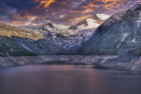 Snowy mountain peaks and a lake at sunset with pink and purple sky, Mattmark reservoir, Saas