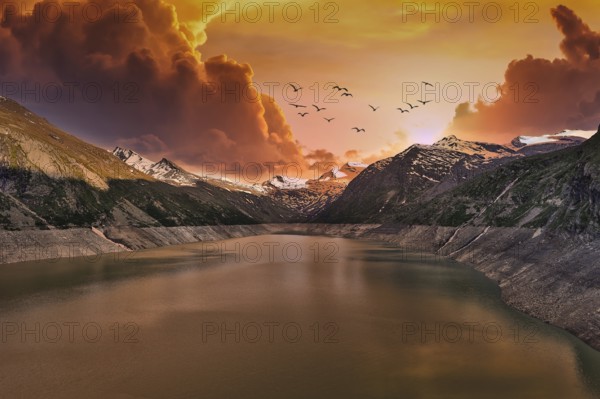 Dramatic sunset over a mountain lake with flying birds and clouds, Mattmark Reservoir, Saas