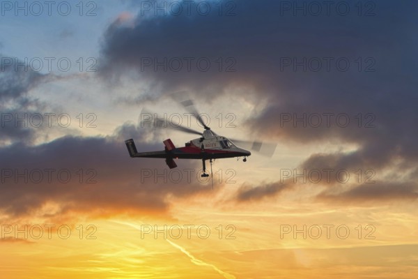 A helicopter flies in front of a dramatic sky with clouds and sunset, transport helicopter, timber