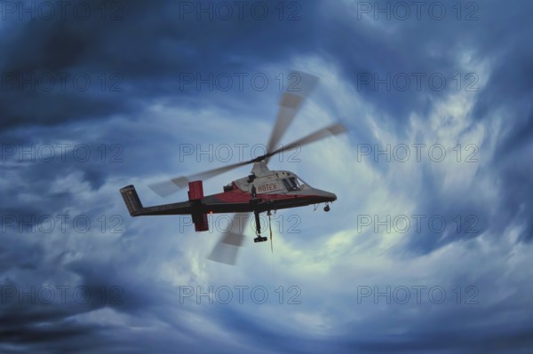 A helicopter flies through a dramatic, stormy blue sky, transport helicopter, timber transport,
