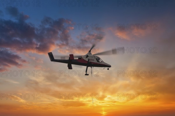 A helicopter hovers elegantly in front of a brightly coloured sunset sky, transport helicopter,