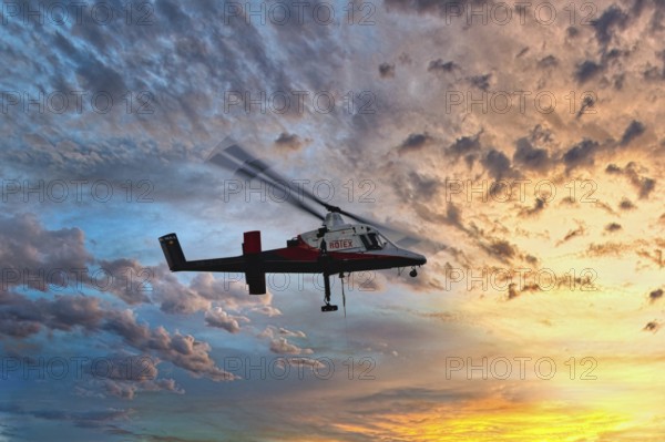 A helicopter flies in front of a colourful sunset with dramatic cloud formations, transport