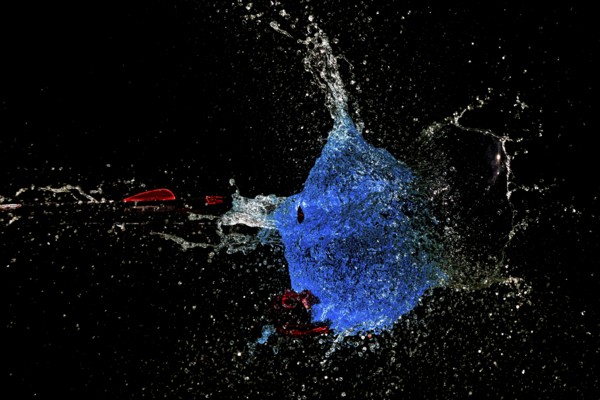 A blue water balloon bursts with force while an arrow shoots through it, surrounded by a dark