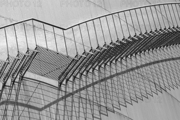 An abstract view of a metal staircase in black and white, emphasised by strong shadow lines,