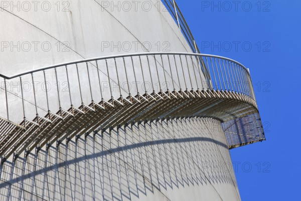 The staircase runs along a large tank in front of a clear blue sky, high tank, chemical, company,