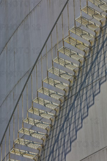 Close-up view of a metal staircase on an industrial gas tank with long shadow lines, elevated tank,
