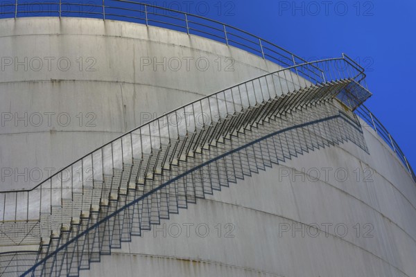 Large, curved metal staircase runs along a tank under a clear sky, elevated tank, chemical,