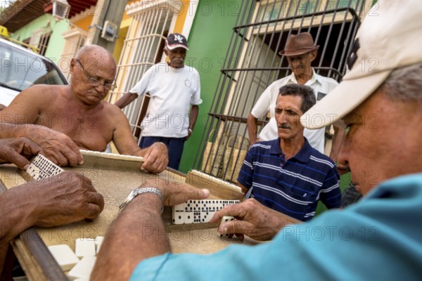 Old Cubans playing dominoes at a table on the street in the city centre of Trinidad, Trinidad,