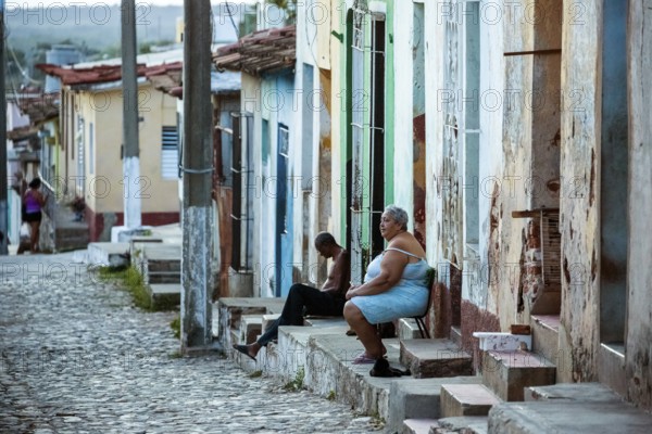 Cubans sitting on their steps in front of their houses in the old town, Street scene in the old