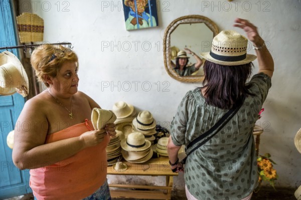 Cuban hat saleswoman with a tourist in a shop in the old town of Trinidad, Trinidad, Cuba, Sancti