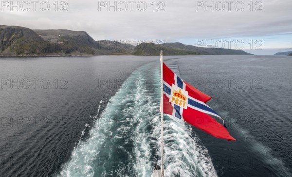 The post symbol on a Norwegian flag of a Hurtigruten ship, foaming spray, Honningsvåg, Finnmark,