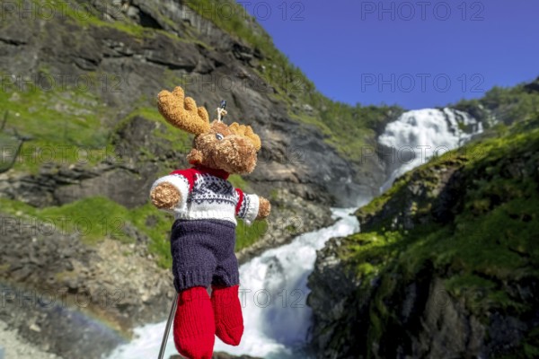 Kjosfossen waterfall, mascot moose in front of waterfall, mountain, rock faces, meadow, sky,