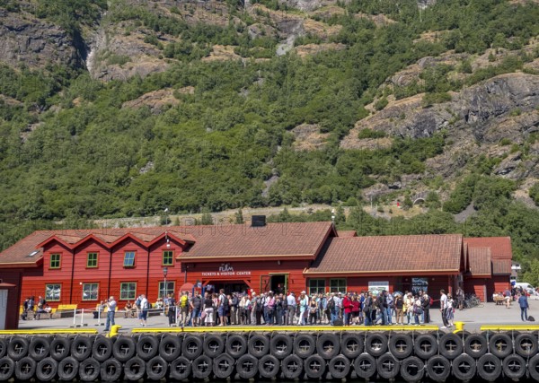 Flåm, tourists at the TICKETS & VISITOR CENTER, red wooden house, landing stage for ships, rock