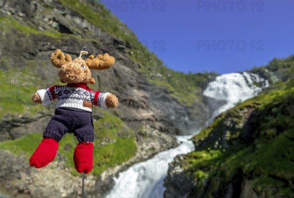 Kjosfossen waterfall, mascot moose in front of waterfall, mountain, rock faces, meadow, sky,