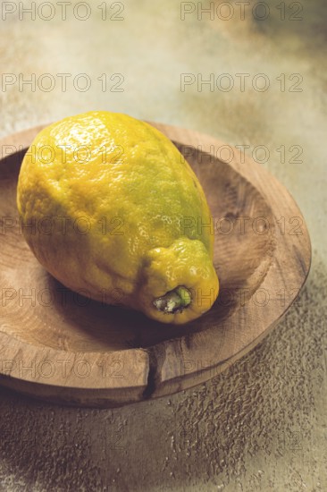 A vibrant lemon sits on a rustic wooden plate, showcasing its uneven texture and vivid color. The