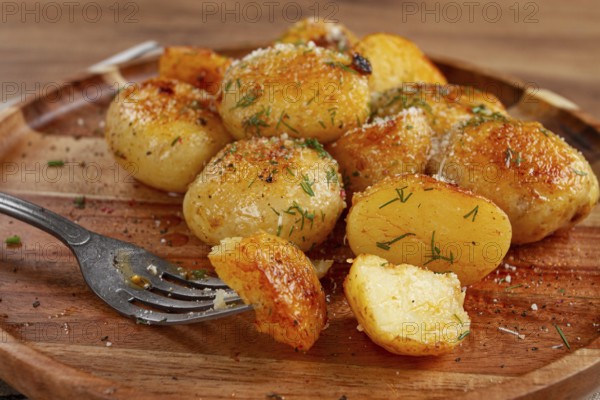 Half-eaten fried new potatoes, with butter and dill, on a wooden plate, with a fork, at home,
