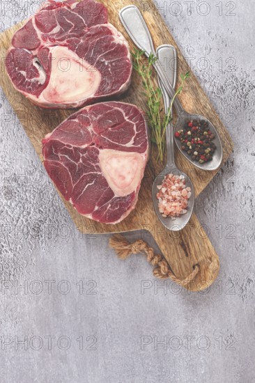 Freshly sliced beef legs, two ossobuco steaks, on a wooden board, with spices and herbs, ready to