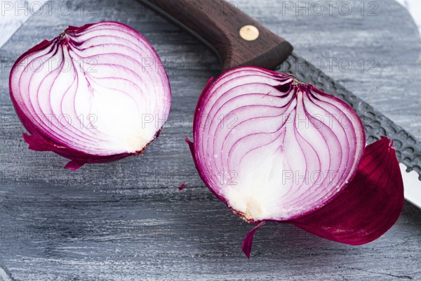 A vibrant red onion is cut in half, on a rustic wooden chopping board beside a sharp knife, ready