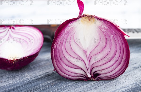 A vibrant red onion is cut in half, on a rustic wooden chopping board beside a sharp knife, ready