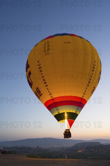 A large, luminous balloon floats over a clear mountainous landscape at dawn, Göreme National Park,