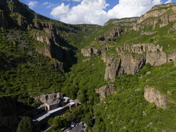 Gorge with lush greenery and rocks under a blue sky with clouds, aerial view, Geghard Monastery,