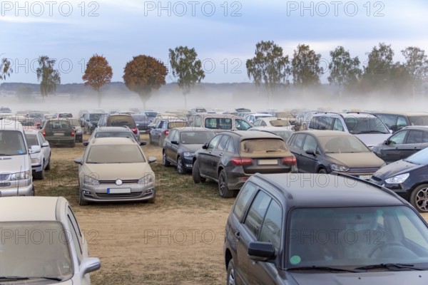 Dusty parking space scenery on a field including lots of dust covered cars at evening time in