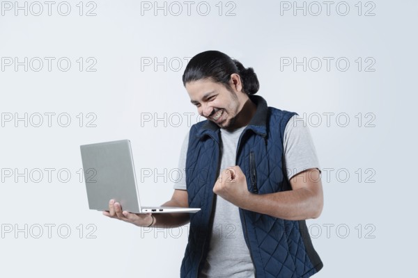 Male celebrating with fist in the air holding a laptop on white background. Young man celebrating