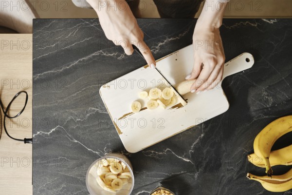 A person slices fresh bananas on a white cutting board in a well-lit kitchen. The countertop