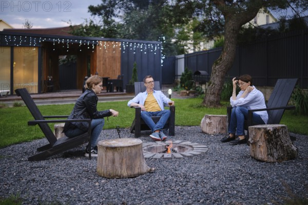A family gather around a small fire pit in a backyard of tiny house, enjoying each their company.