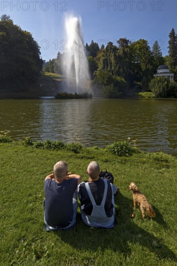 Couple with dog at the water games at the big pond with the high rising fountain, Bergpark