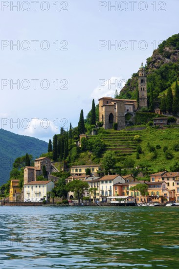 House and Church on Mountain Range in a Sunny Summer Day on the Waterfront to Lake Lugano in