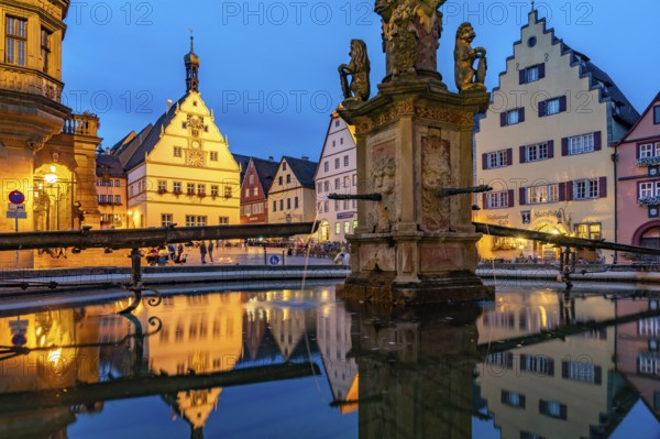 The market square with the Ratstrinkstube is reflected in the Georgsbrunnen fountain at dusk,