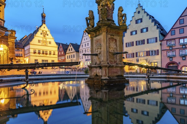 The market square with the Ratstrinkstube is reflected in the Georgsbrunnen fountain at dusk,