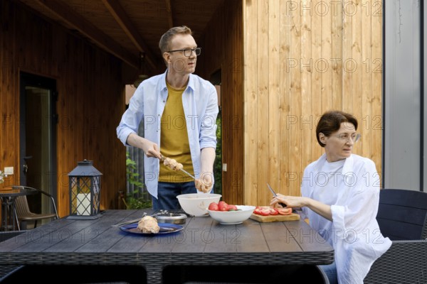 During a sunny day a couple is engaged in preparing a meal outdoors. One person is skewering food