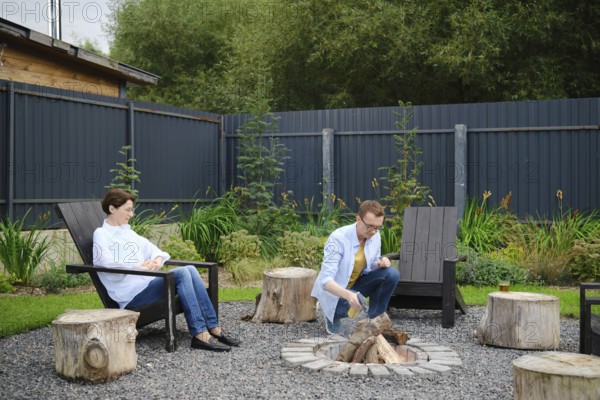 Middle-aged couple enjoy a relaxing evening in a backyard, sitting by a campfire surrounded by